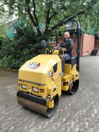 Ein Parkmitarbeiter sitzt auf der neuen Wegewalze und freut sich über die Neuanschaffung